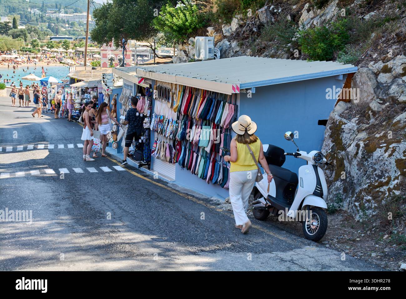 Corfù. Grecia - 22 gennaio 2026: Una vivace scena di strada a Corfù che mostra un negozio di souvenir locale con borse tote colorate, turisti che navigano e un po' Foto Stock