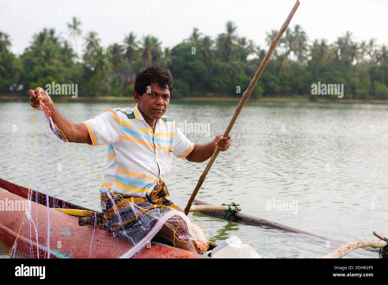 Ritratto di un pescatore seduto su una tradizionale barca da pesca stretta nella baia costiera dello Sri Lanka. Autentico stile di vita marittimo, tradizionale cultura della pesca Foto Stock