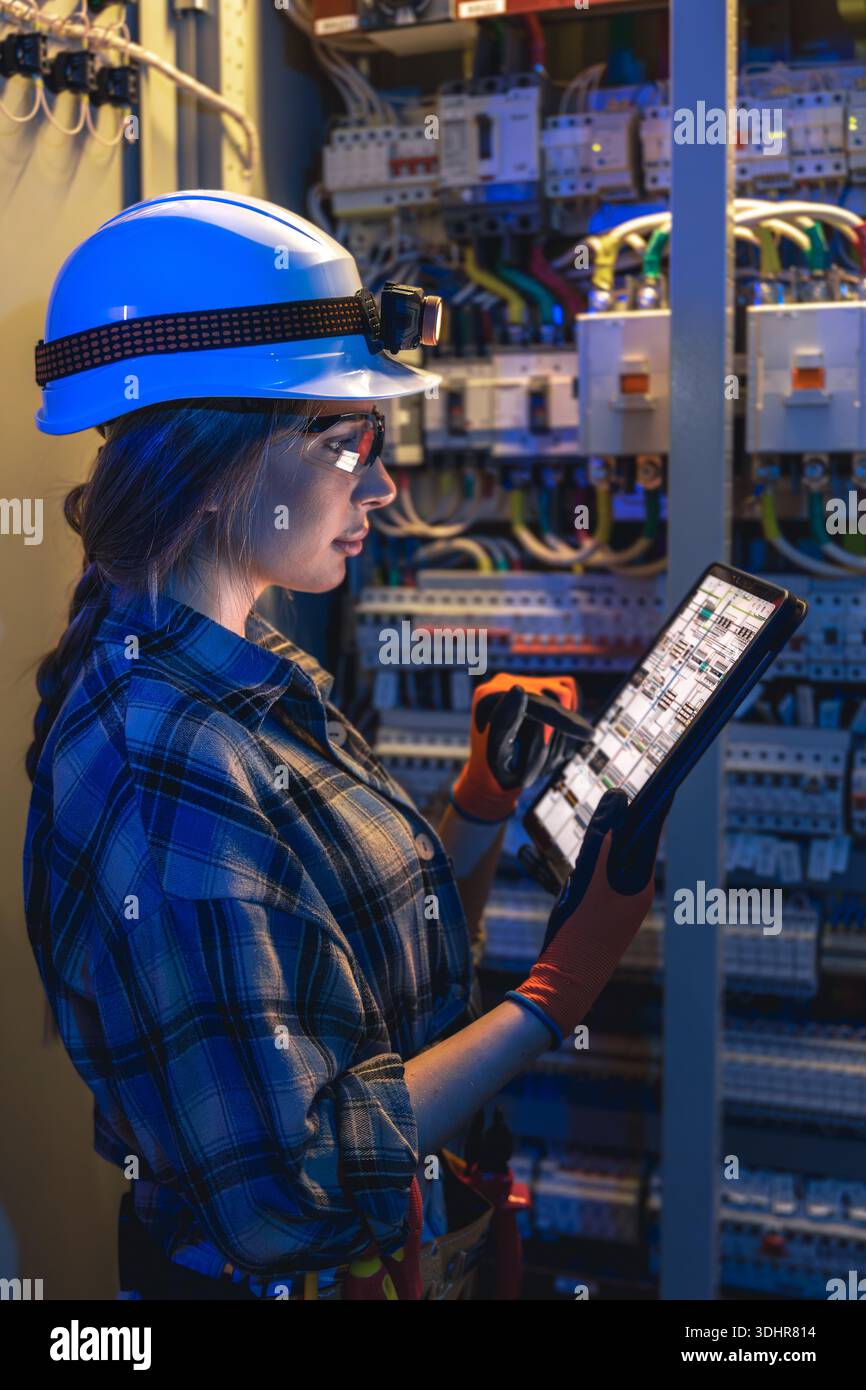 Una donna elettricista legge gli schemi dei tablet tramite il gruppo di comando. Ispezione digitale. Foto Stock