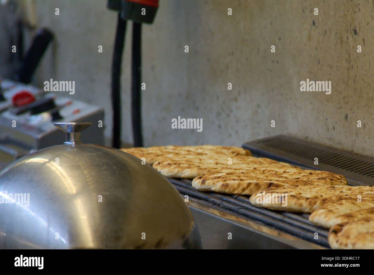 Primo piano del tradizionale pane pita greco tostato su una griglia di metallo all'interno di una cucina commerciale a Corfù, Grecia. Foto Stock
