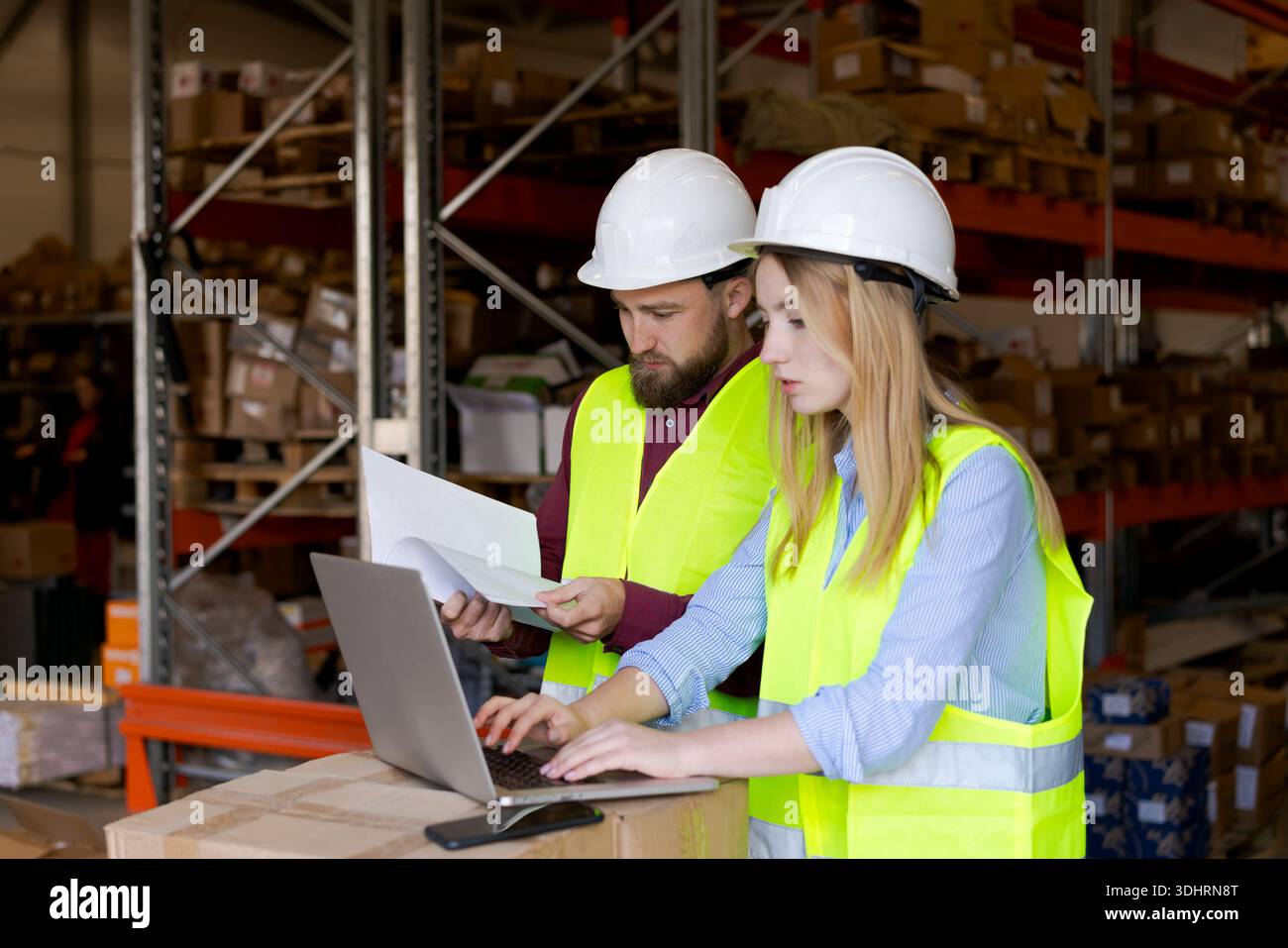 Lavoratore di sesso maschile che esamina il documento mentre un collega di sesso femminile elabora le informazioni sul laptop. Business intelligence e metriche di performance nella mana logistica Foto Stock