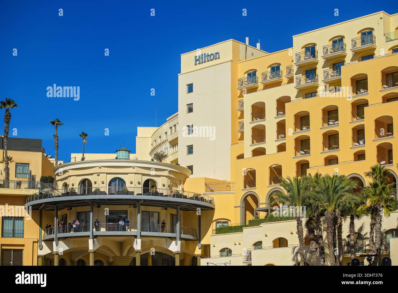 St. Julians, Malta - 3 novembre 2025: Un bellissimo e moderno edificio alberghiero Hilton di lusso caratterizzato da una facciata gialla, balconi e palme Foto Stock