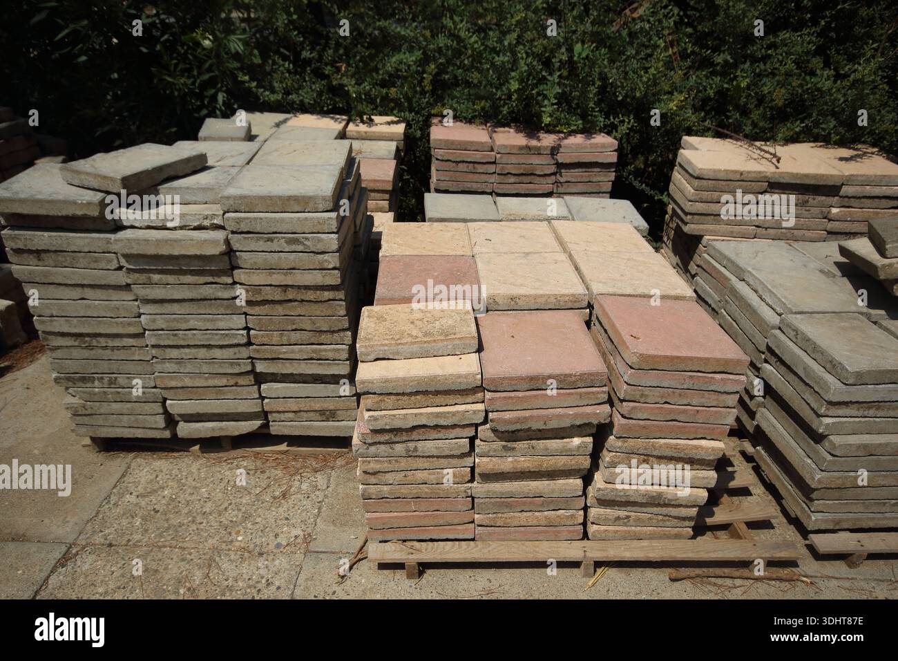 Lastre di pavimentazione in calcestruzzo quadrate impilate in toni grigi e di terracotta su pallet in legno per la paesaggistica Foto Stock