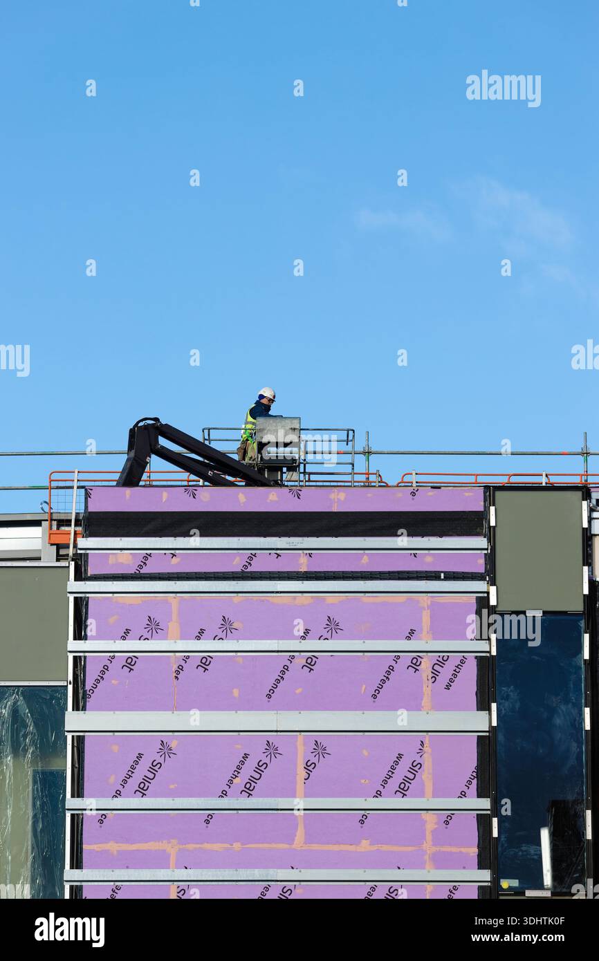 Operaio edile sul braccio di sollevamento sopra il tetto dell'edificio del mozzo Radcliffe, pannello di rivestimento esterno, guide di supporto in acciaio zincato, Greater manchester uk Foto Stock