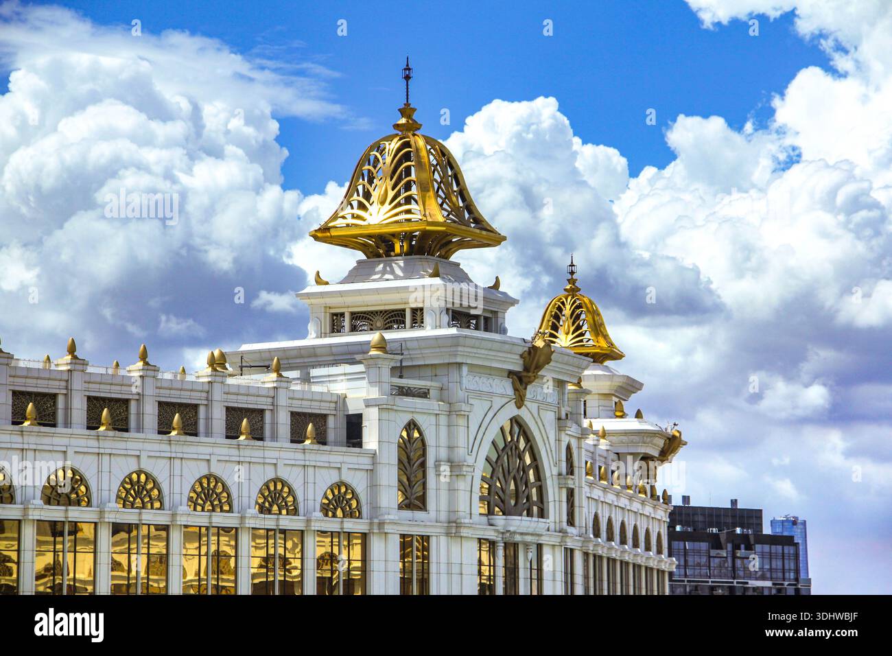 Opulento edificio in marmo bianco caratterizzato da intricate cupole dorate e da un'architettura dorata ornata sotto un cielo blu con spettacolari nuvole bianche. Foto Stock