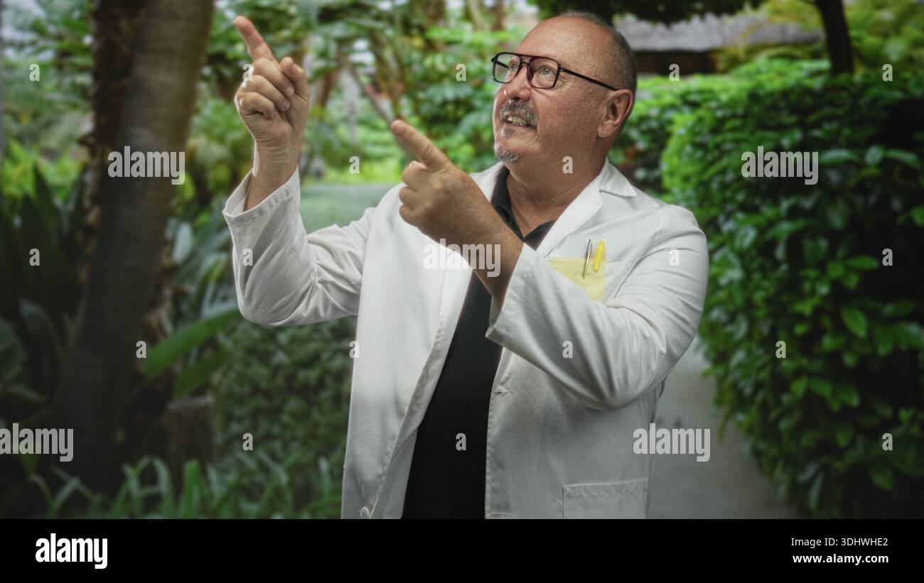 Uomo medico, ispanico anziano nel camice da laboratorio punta il dito verso l'alto con entrambe le mani vicino al passaggio del giardino, costruendo, indossando occhiali e penne tascabili; curiosit Foto Stock