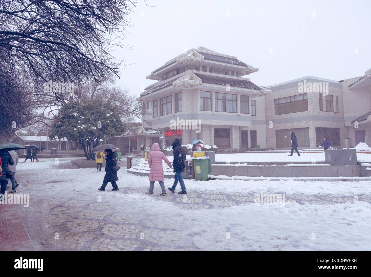 I visitatori camminano attraverso una piazza coperta di neve verso un negozio di souvenir presso il Mausoleo dell'Imperatore Qinshihuang a Xi'an Foto Stock