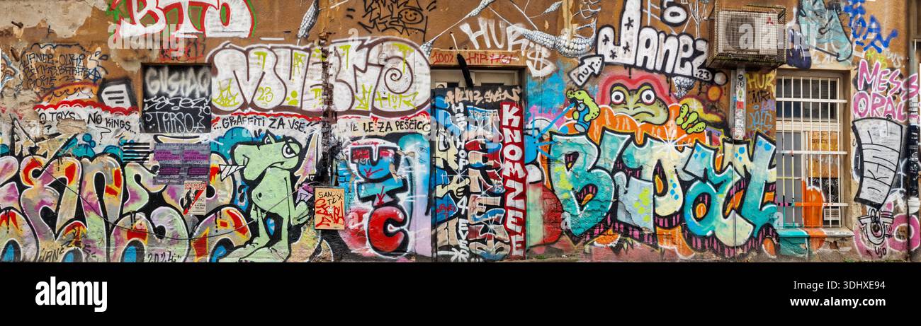 LUBIANA, SLOVENIA — 23 dicembre 2025: Ampio panorama di murales creativi e installazioni d'arte sotterranea nello storico quartiere di Metelkova. Foto Stock