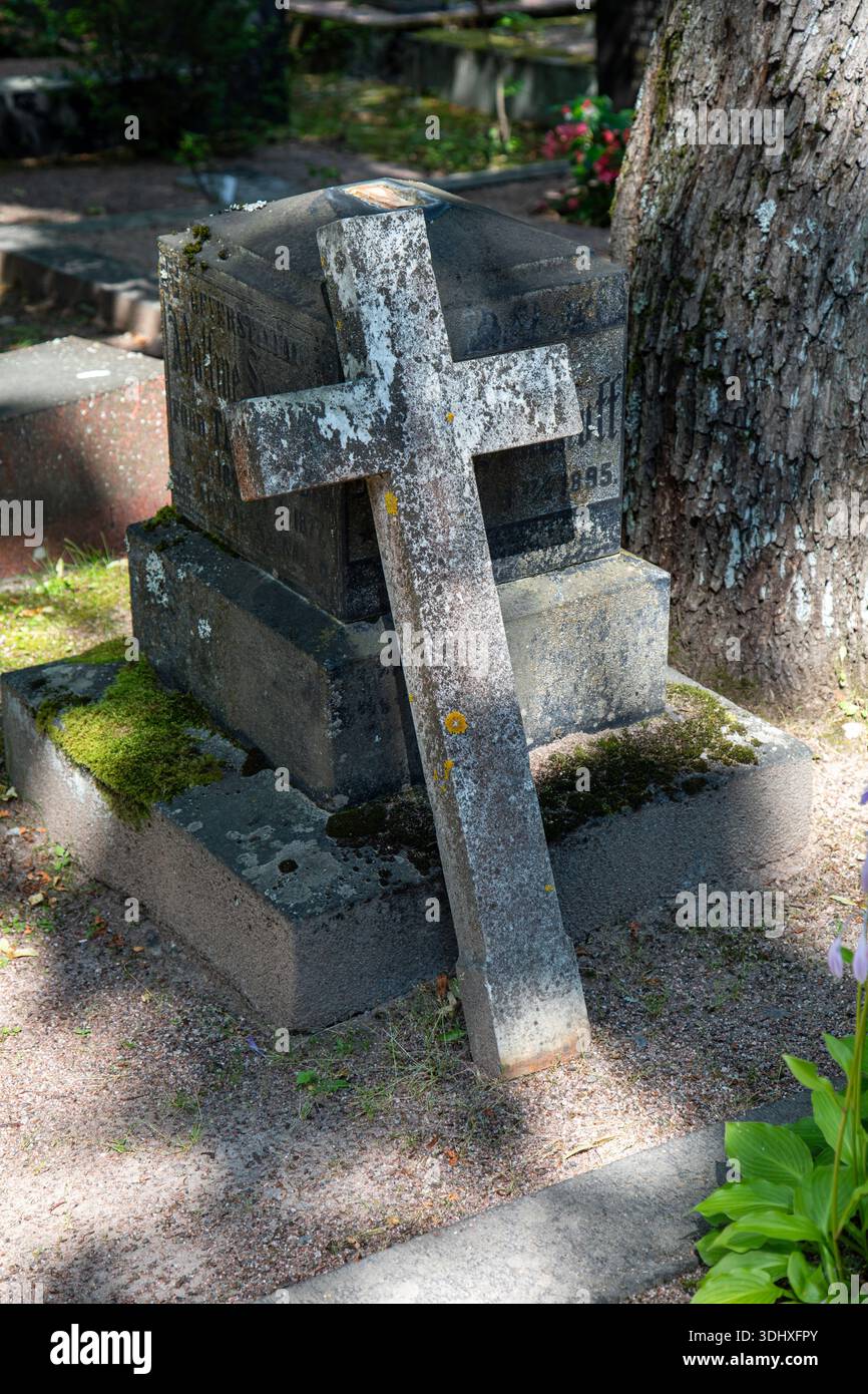 Croce in pietra ricoperta di licheni appoggiata alla lapide del cimitero Hietaniemi di Helsinki, Finlandia Foto Stock