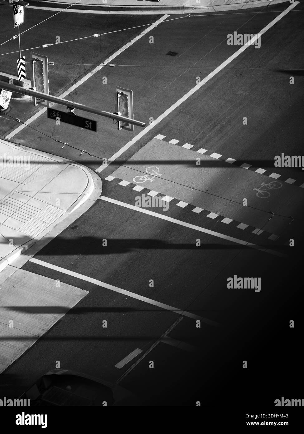 Un pulito incrocio urbano in bianco e nero presenta una pista ciclabile che attraversa la strada, contrassegnata da simboli bianchi e delimitata da linee tratteggiate. Foto Stock