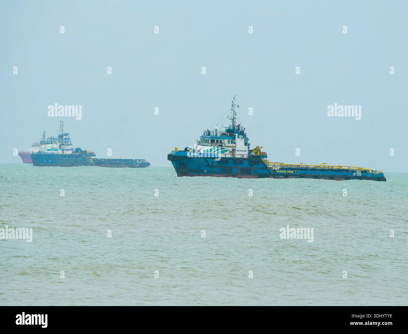 Due grandi navi di rifornimento offshore industriali ancorate in acque costiere verdeggianti sotto un cielo confuso e coperto. Perfetto per temi marittimi e di spedizione. Foto Stock
