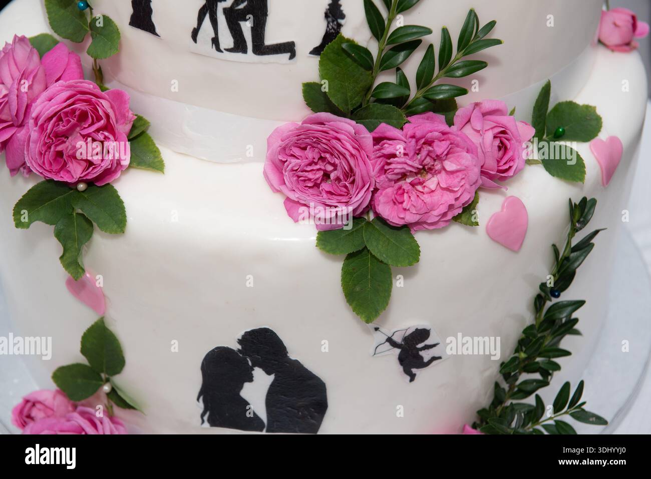 primo piano di una torta nuziale decorata con un tema romantico. I dettagli principali includono: Si tratta di una torta a più livelli con glassa bianca liscia. Foto Stock