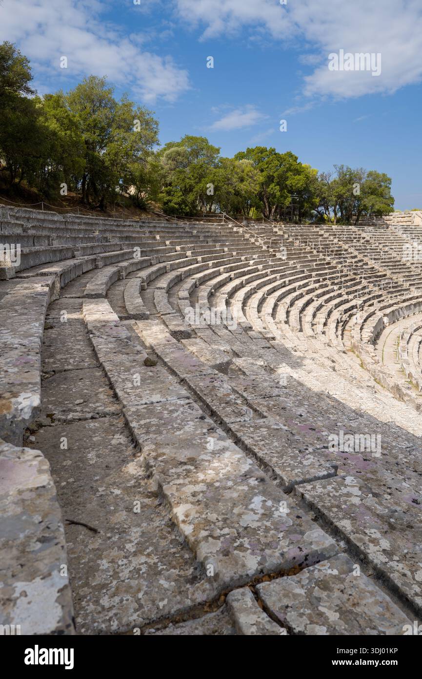 Epidauro, Grecia - 2 settembre 2024: Vista ravvicinata delle file di pietra e dei gradini dell'antico teatro semicircolare del Santuario di Asclepio, con alberi circostanti e un cielo parzialmente nuvoloso visibile. Foto Stock