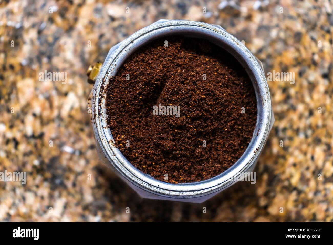 Primo piano dall'alto di un classico imbuto per moka italiana riempito con polvere di caffè appena macinato, pronto per essere estratto su un piano di granito. Un simbolo o. Foto Stock