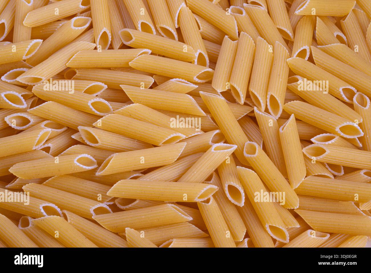 penne grezze da primo piano con consistenza ruvida di semola, tubi dorati ben confezionati che formano pattern ripetitivi, ideali per il confezionamento di alimenti, il design dello sfondo, Foto Stock