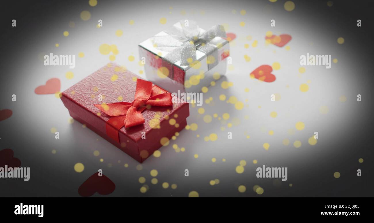 Mostra due regali avvolti su un tavolo bianco, scatola rossa testurizzata, scatola d'argento, coriandoli a cuore, bokeh dorato Foto Stock