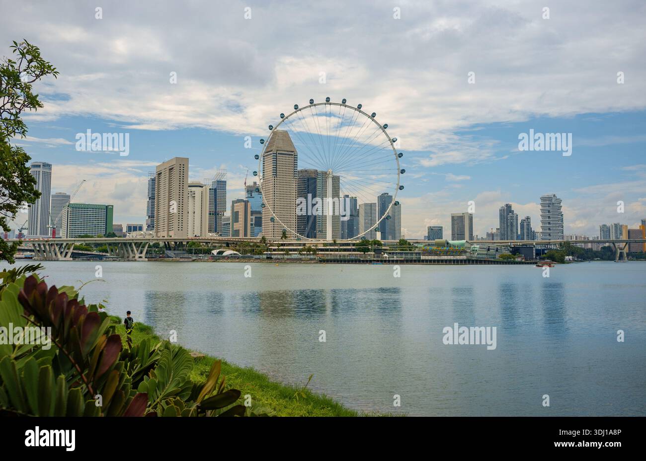 Il Singapore Flyer visto attraverso il bacino idrico di Marina Bay con i grattacieli dello skyline di Singapore catturati al tramonto Foto Stock