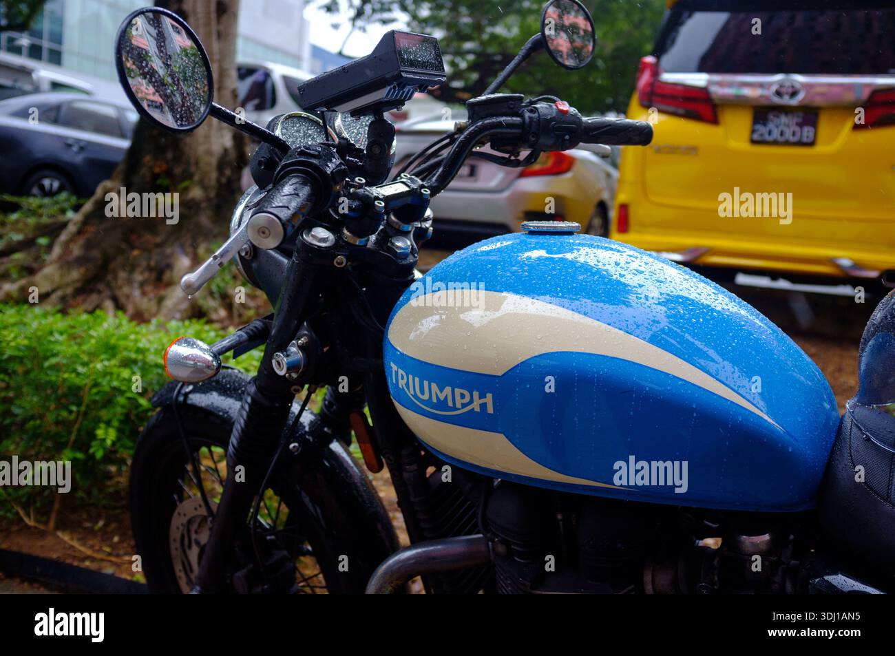 Un primo piano di Triumph Bonneville con serbatoio carburante blu e maniglie parcheggiate in strada con la pioggia sotto forma di goccioline a Singapore in Asia. Foto Stock