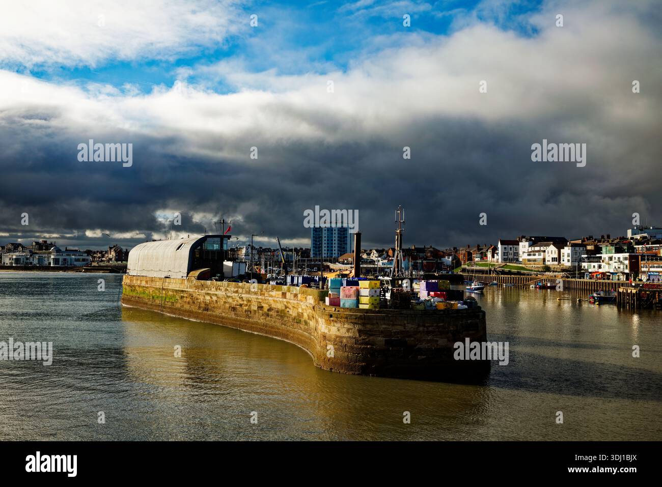 Una riva di nuvole di pioggia scure sopra lo skyline di Bridlington con il molo del porto illuminato dal sole in primo piano, East Yorkshire, Inghilterra. Foto Stock
