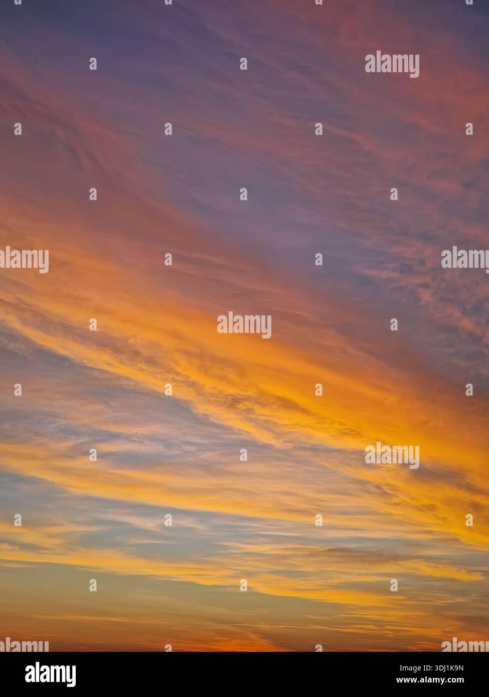 Cielo luminoso al tramonto con strati multicolori di nuvole testurizzate. L'orizzonte si illumina di una luce arancione e gialla ardente, mentre l'atmosfera superiore transita Foto Stock