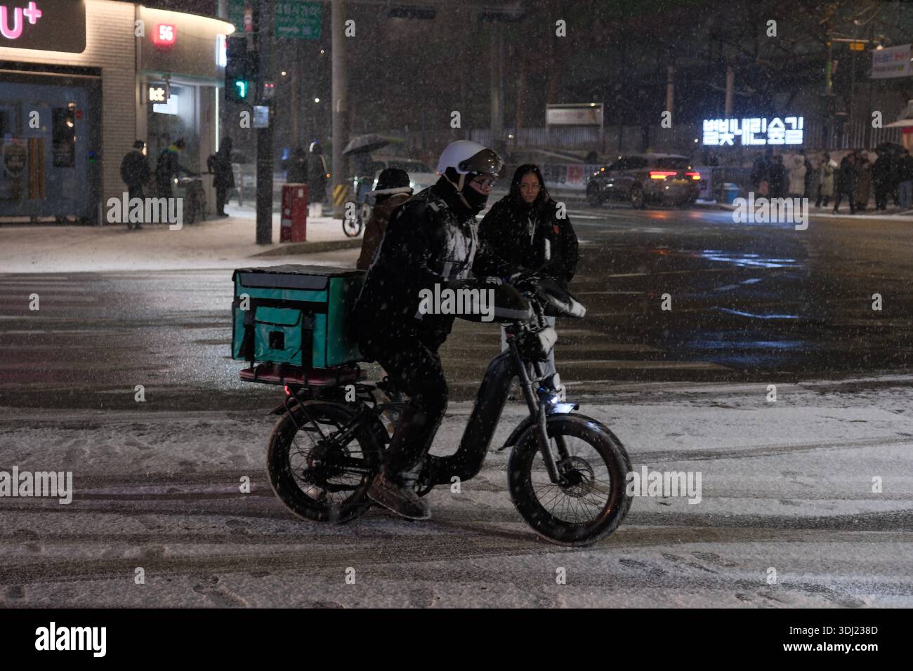 Seoul, Corea del Sud: Consegna di cibo a corriere in bicicletta elettrica durante le forti nevicate all'incrocio notturno Foto Stock