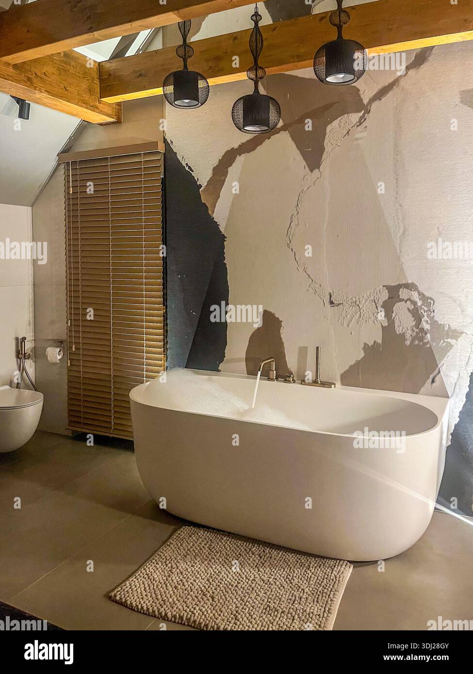 Moderna vasca da bagno bianca riempita di schiuma in un bagno elegante, con travi in legno, lampade a sospensione e un esclusivo design a parete testurizzato con copia Foto Stock