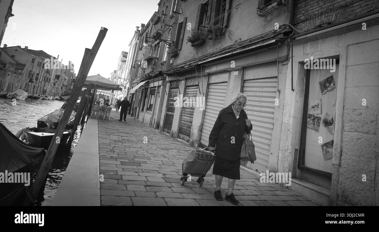 Cannaregio Venice Street, donna anziana che porta ad omero il suo shopping, la vita dura Italia Foto Stock