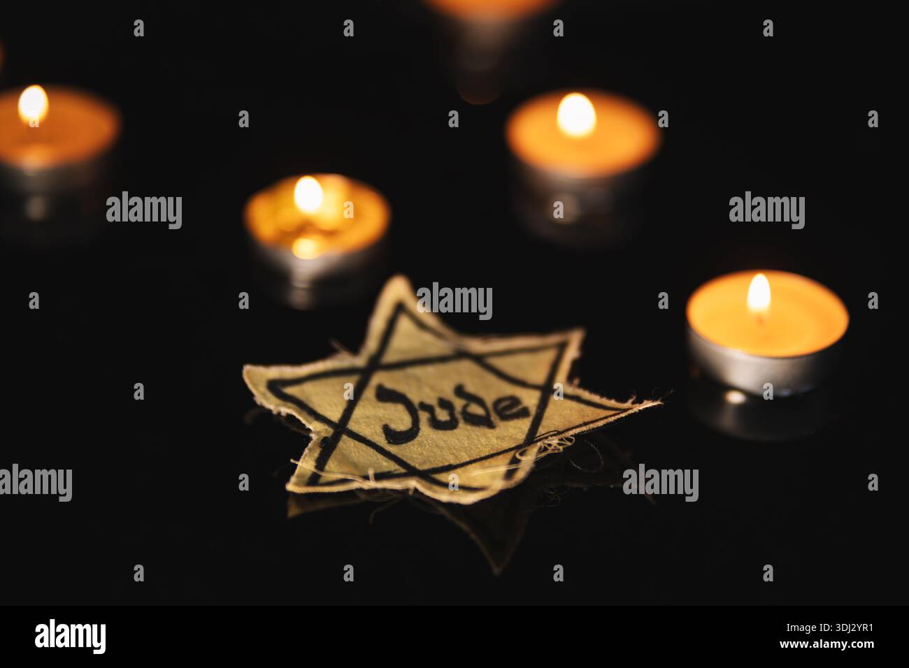 Un distintivo della Stella di David, come quelli indossati con la forza dagli ebrei nei ghetti durante la persecuzione, collocato accanto alle candele commemorative accese al buio, che commemorano H. Foto Stock