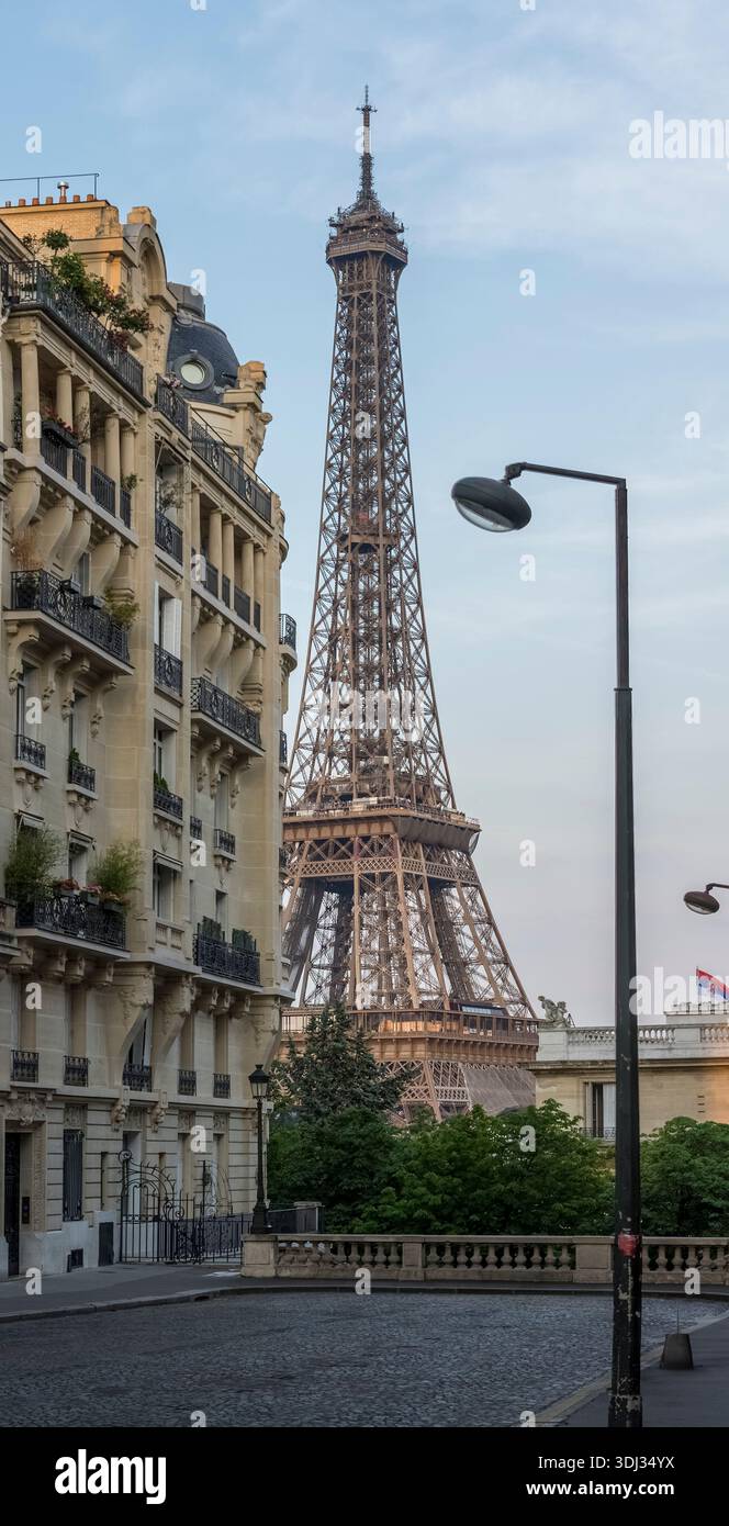 La Torre Eiffel si erge sopra i classici edifici residenziali parigini, vista da una tranquilla strada lastricata del quartiere di Parigi, in Francia. Foto Stock