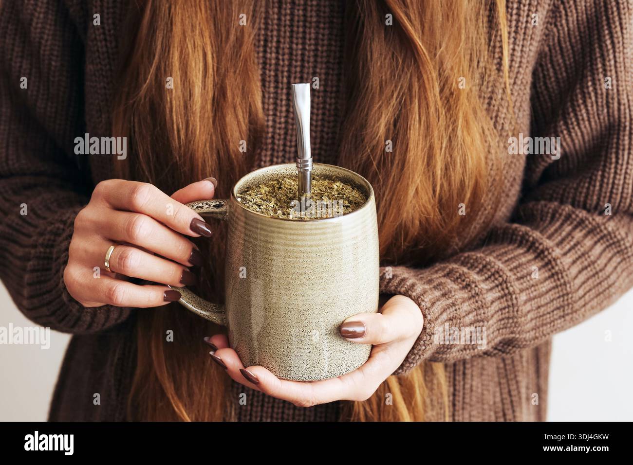 Preparazione della bevanda Yerba mate. Mani che trattengono la zucca con la paglia metallica. Bevanda tradizionale sudamericana. Primo piano di infusione di erbe. Accogliente stile di vita al coperto Foto Stock