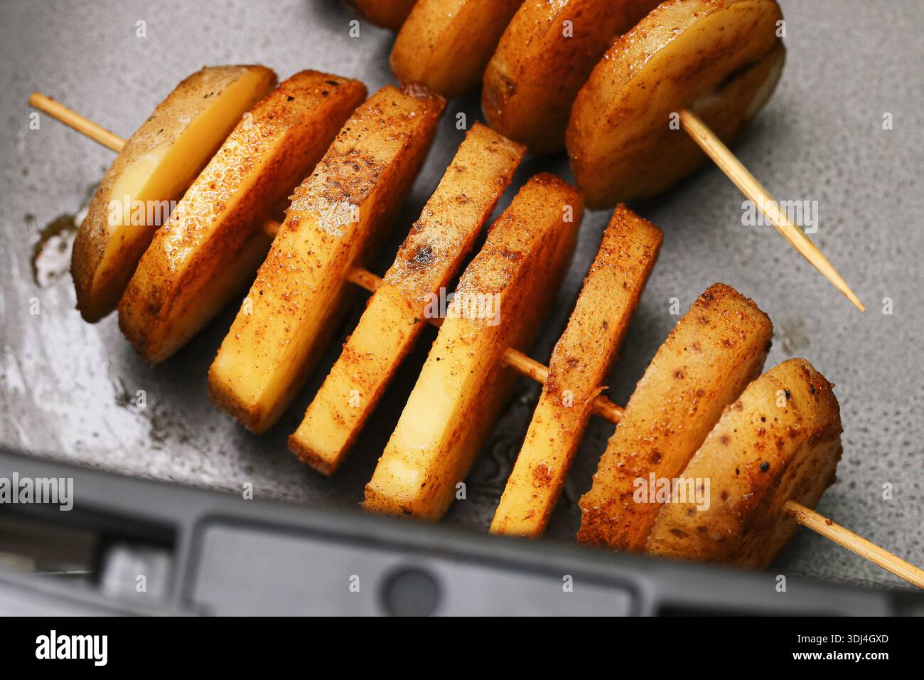 Le patate condite a spirale sugli spiedini di legno. Patate crude a fette preparate per la cottura in forno o in friggitrice ad aria. Snack fatti in casa. Cibo rustico da cucina. Foto Stock