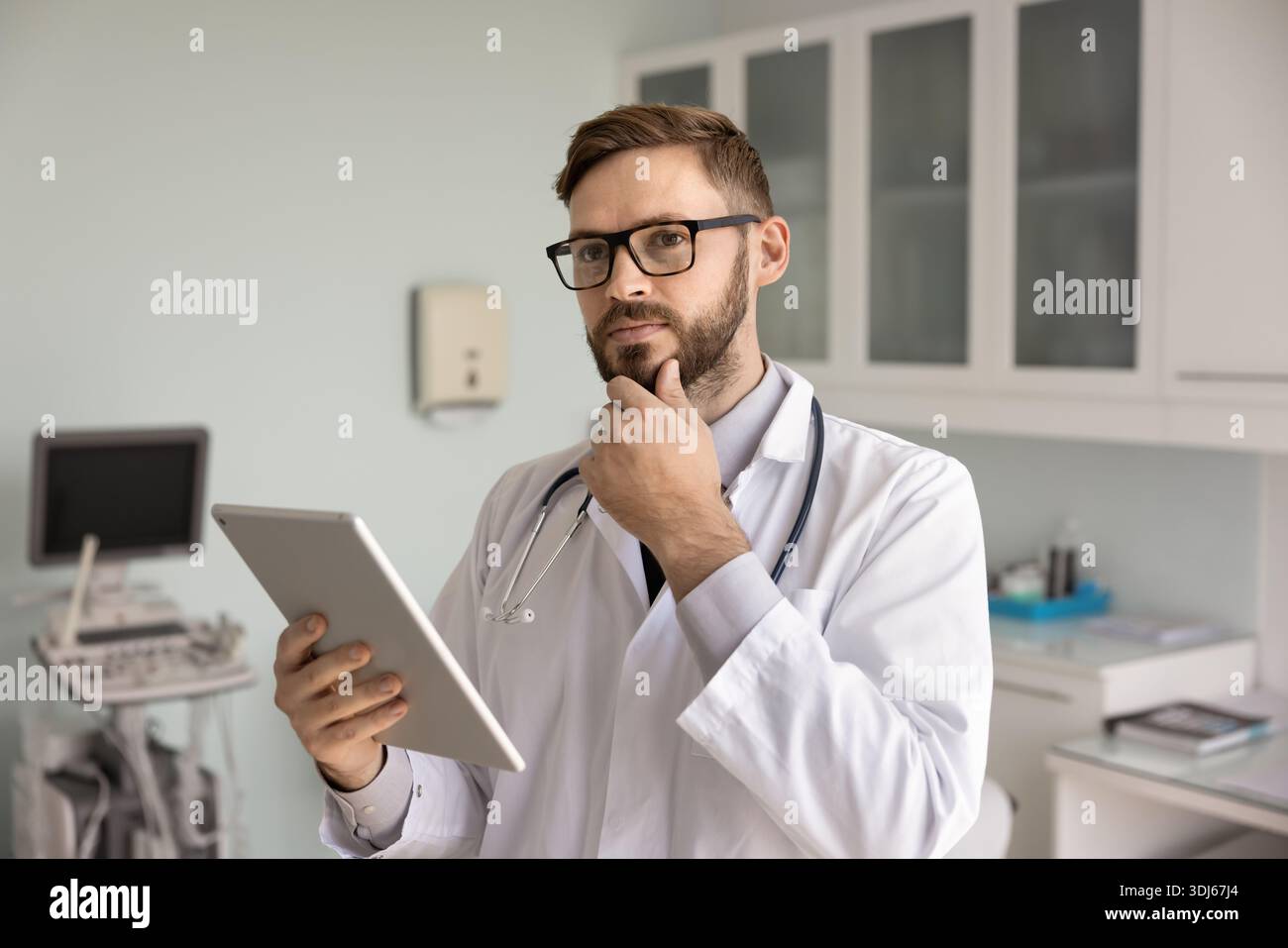 Medico maschile pensivo che pensa in sala esame tenendo un tablet digitale Foto Stock