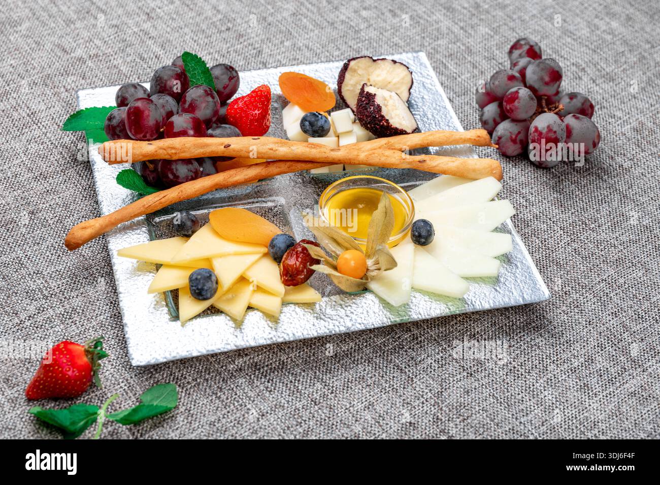 Un vassoio di formaggi gourmet splendidamente organizzato con vari tipi di formaggio a fette, uva rossa, fragole fresche, mirtilli, fisti, e dri Foto Stock