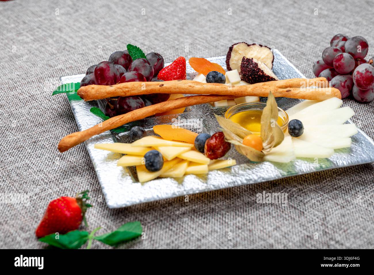 Un vassoio di formaggi gourmet splendidamente organizzato con vari tipi di formaggio a fette, uva rossa, fragole fresche, mirtilli, fisti, e dri Foto Stock