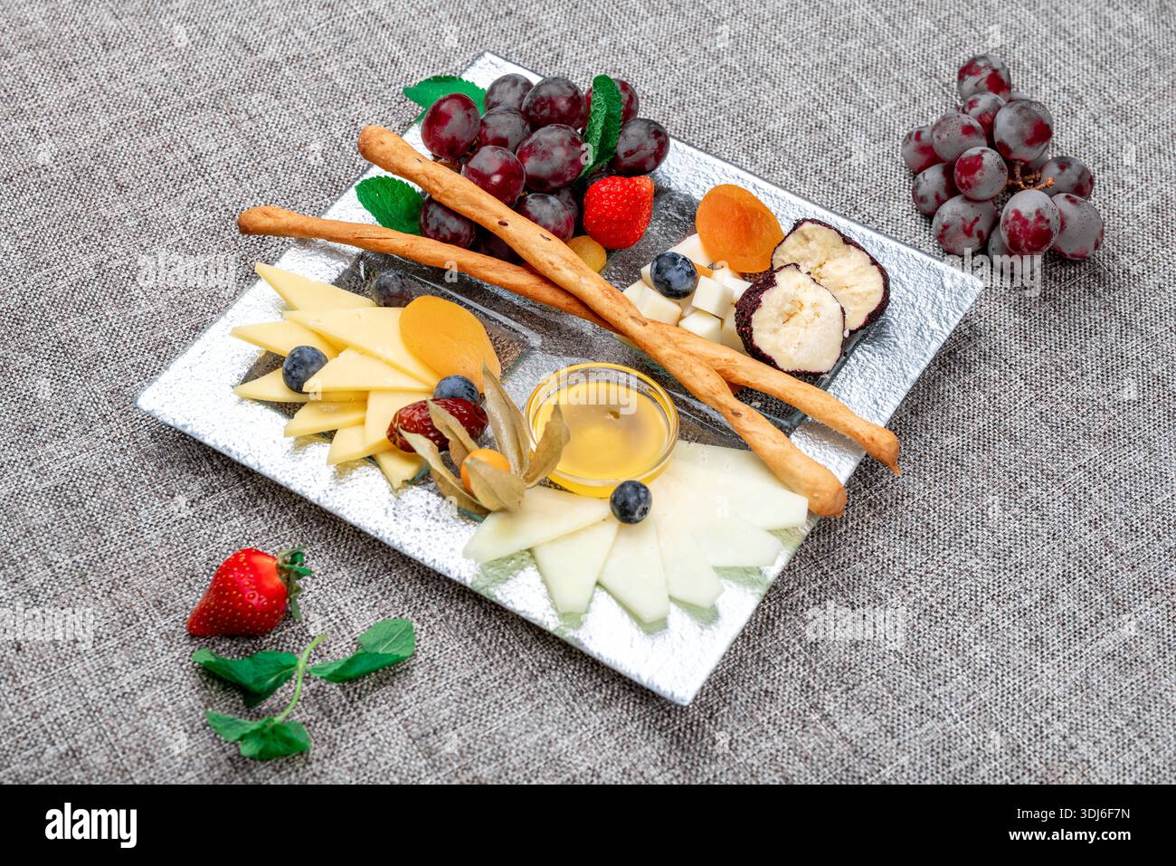 Un vassoio di formaggi gourmet splendidamente organizzato con vari tipi di formaggio a fette, uva rossa, fragole fresche, mirtilli, fisti, e dri Foto Stock