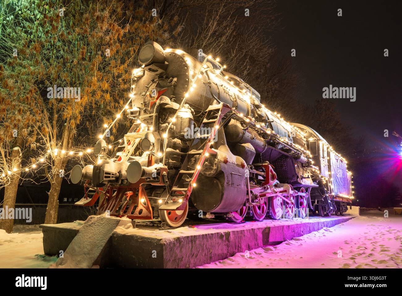 Ulyanovsk, Russia - 14 febbraio 2022: Un vecchio treno decorato con luci multicolore di Capodanno. Strada ricoperta di neve con decorazioni natalizie Foto Stock