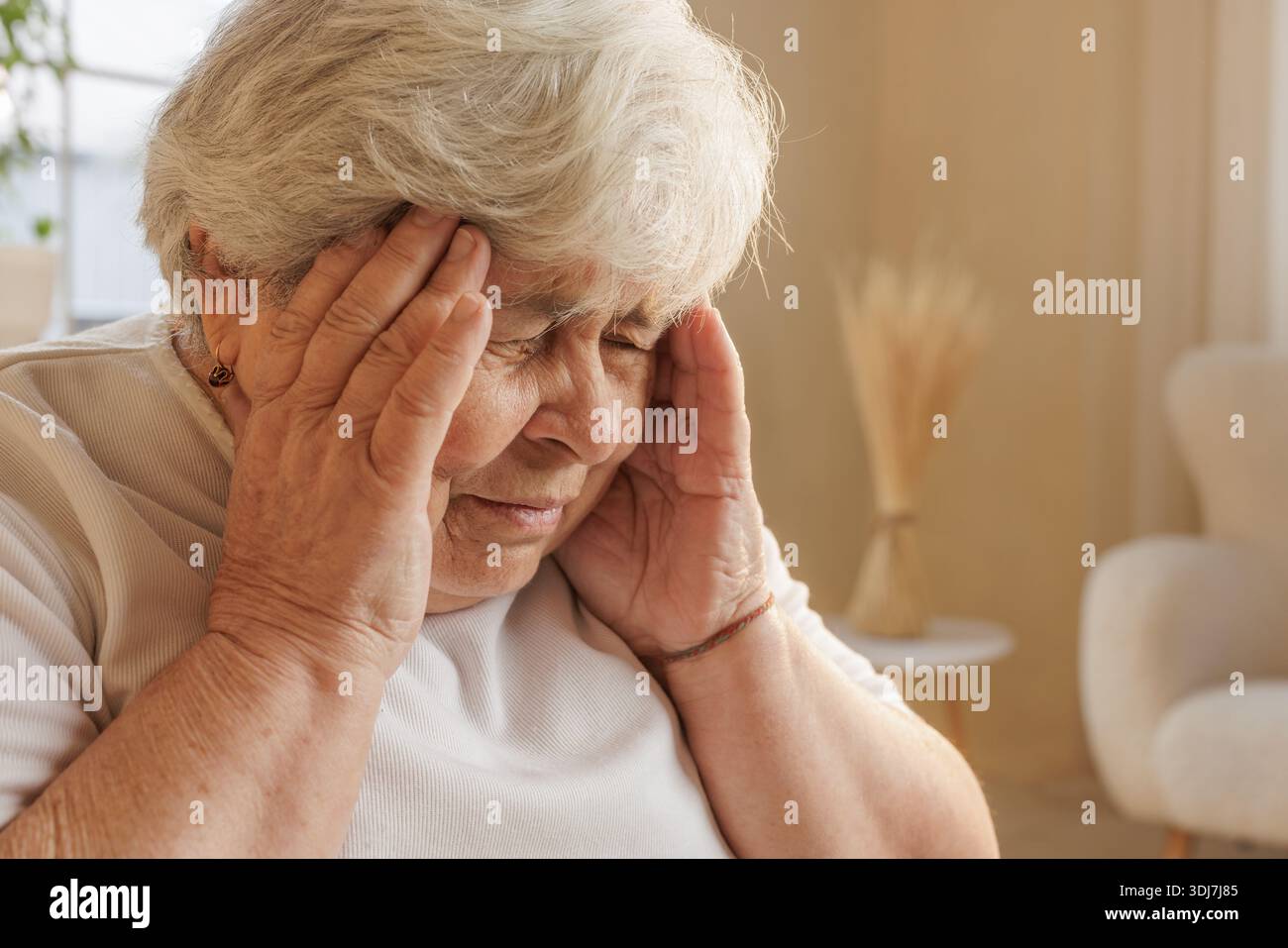 Primo piano di una donna anziana che tocca i templi, soffre di mal di testa o emicrania a casa, occhi chiusi nel dolore. Foto Stock