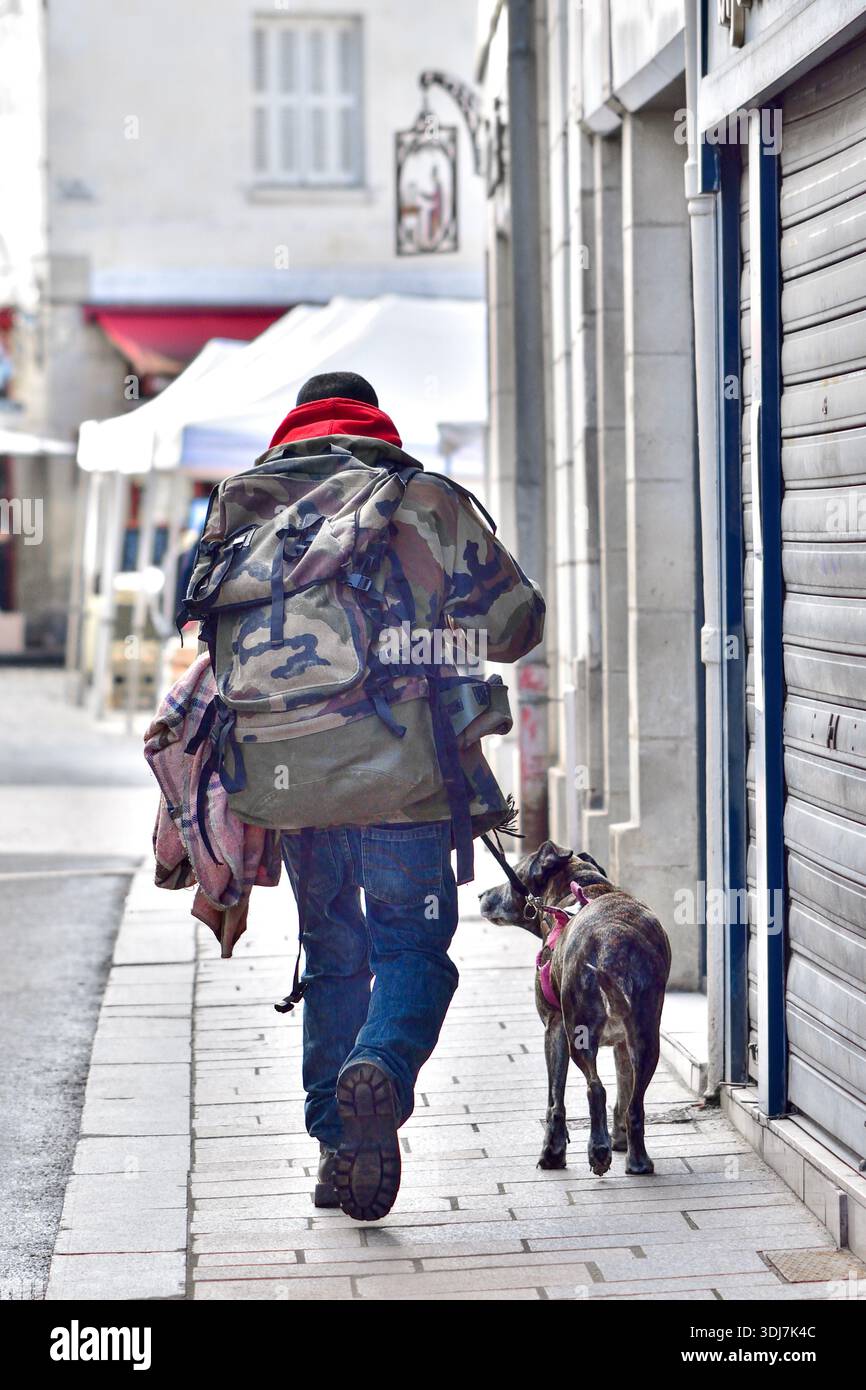 Uomo (possibilmente senzatetto) con zaino grande che cammina per il centro città con cane al guinzaglio - Loches, Indre-et-Loire (37), Francia. Foto Stock