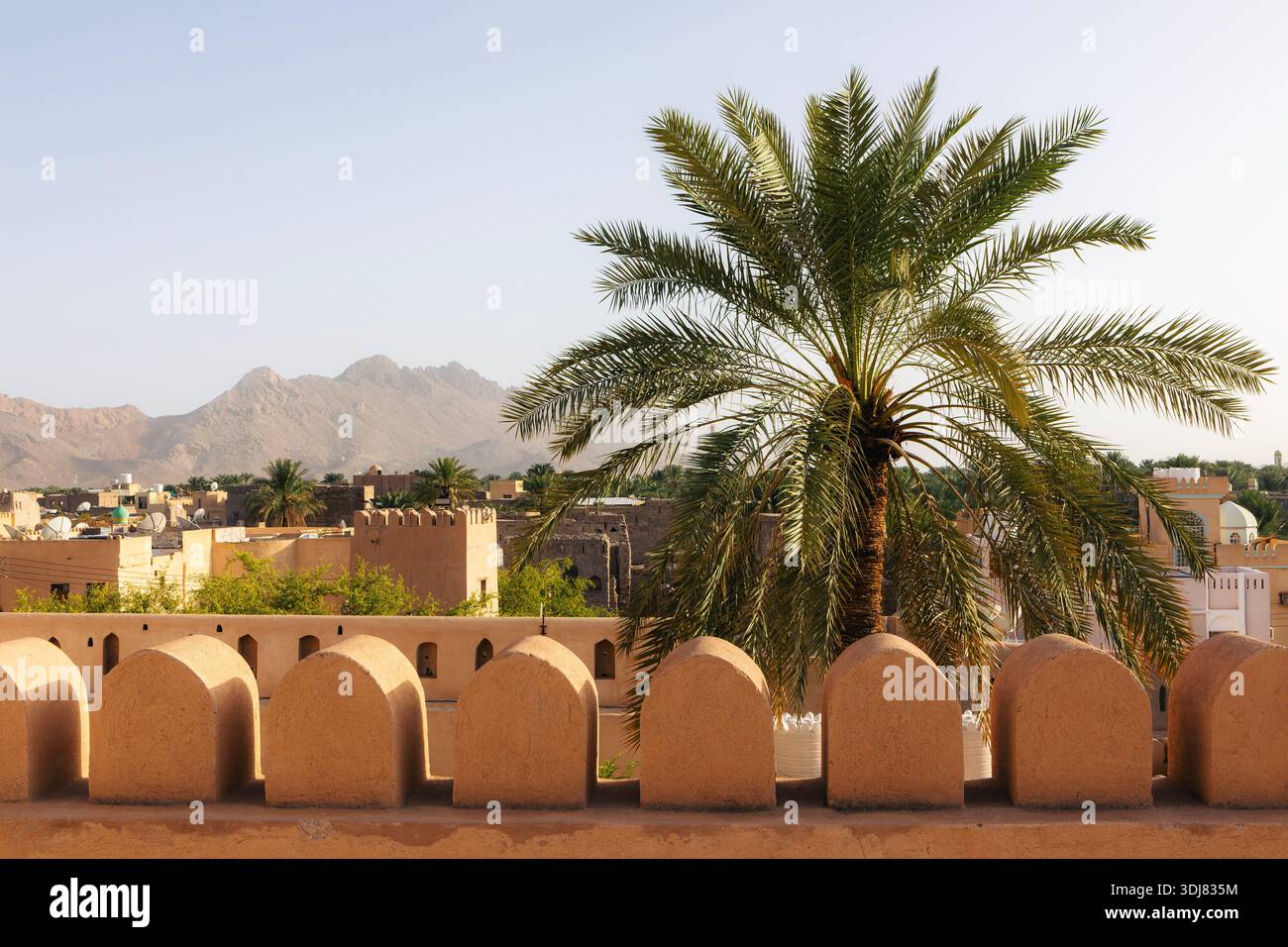 Vista delle mura del forte di Nizwa con la città fredda sullo sfondo di Nizwa, Oman. Architettura difensiva storica, paesaggio urbano e tradizionale mediorientale Foto Stock