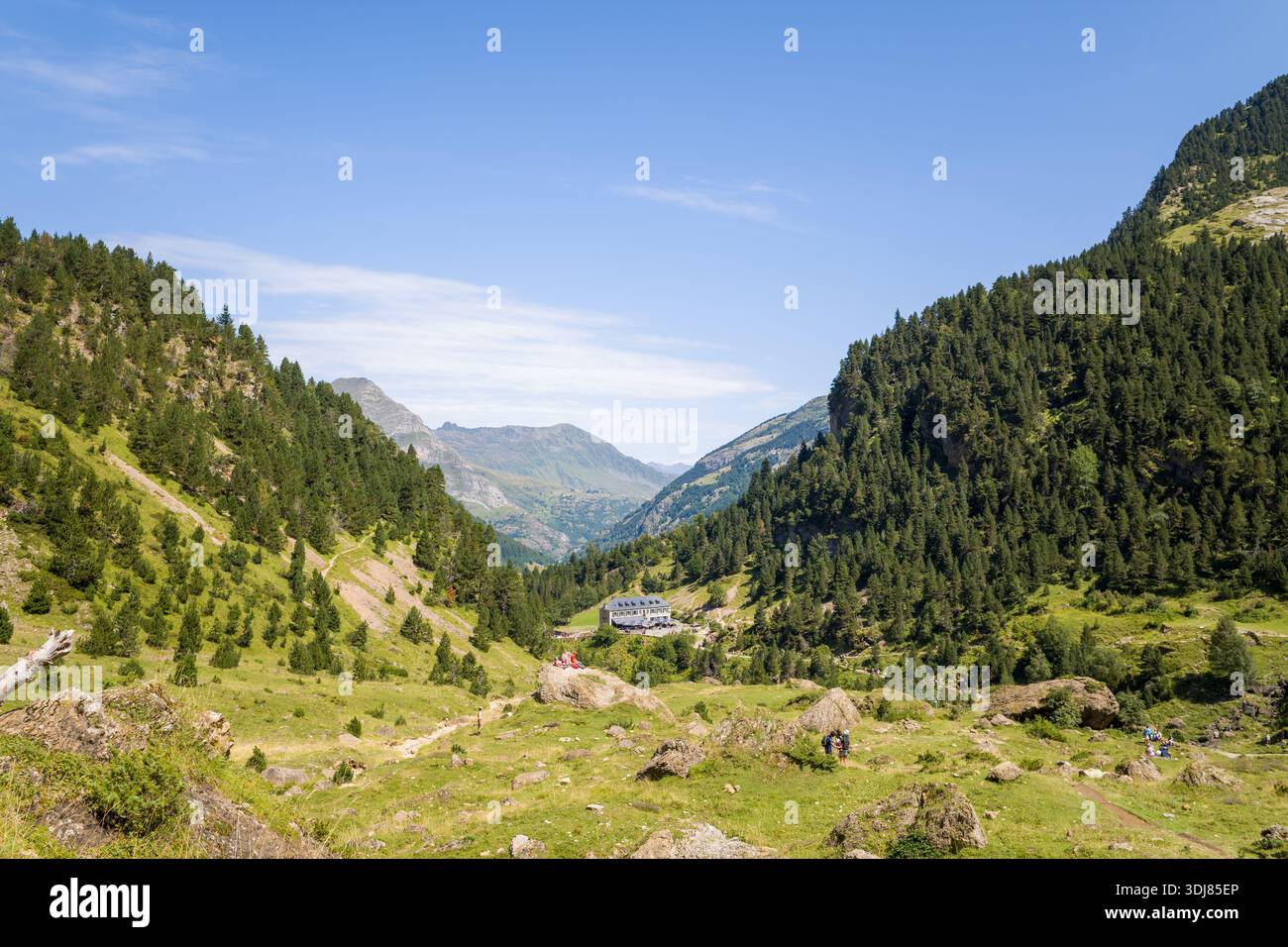 Rifugio du Cirque de Gavarnie, Francia - 9 agosto 2022: Una vista dell'edificio del rifugio di montagna circondato da verdi pendii boscosi e terreni rocciosi, con gruppi di escursionisti visibili lungo la valle sotto un cielo azzurro. Foto Stock