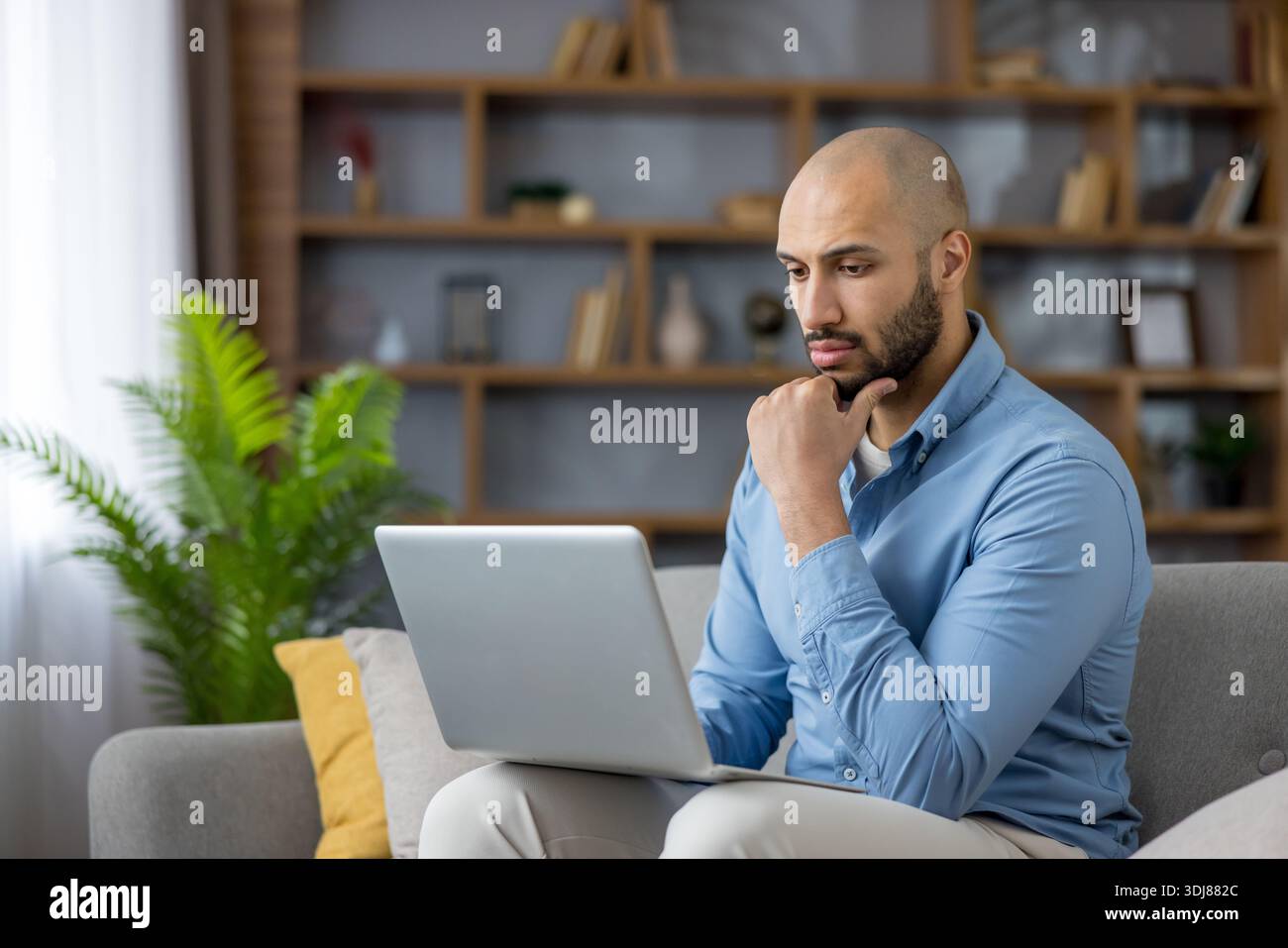 Giovane che si concentra sul laptop, prende decisioni o risolve problemi, catturando l'essenza del lavoro remoto e dell'innovazione digitale in un ambiente domestico contemporaneo Foto Stock