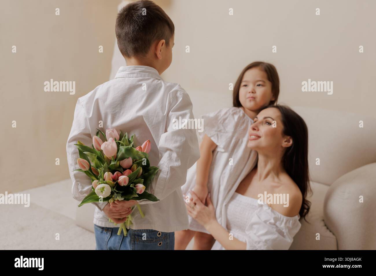 Il figlio amorevole sorprende la madre con i tulipani, celebrando la festa della mamma in un ambiente accogliente, catturando l'amore, la gratitudine e la connessione emotiva della famiglia. Foto Stock
