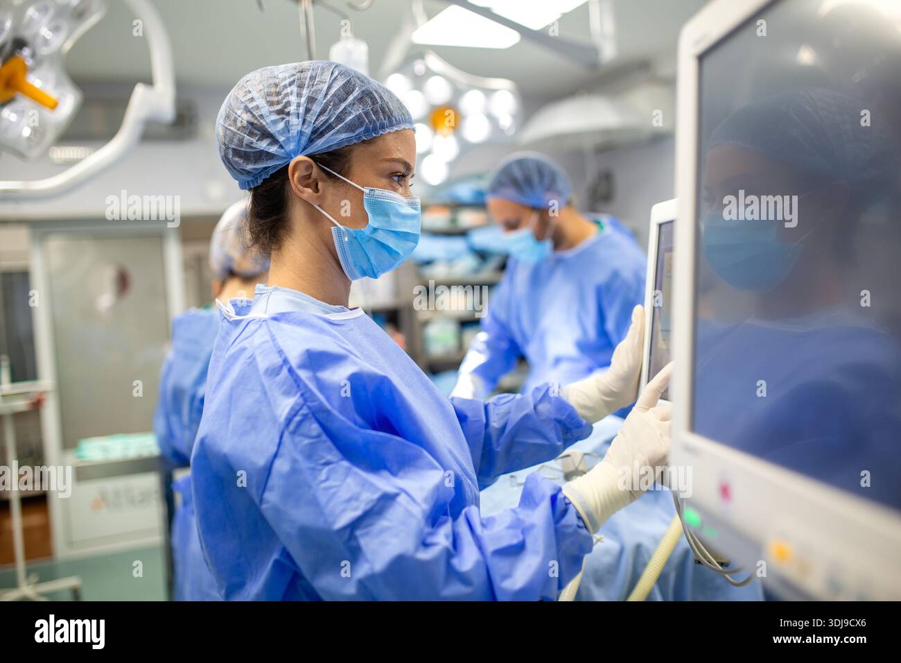 Anestesista che monitora i segni vitali del paziente durante l'intervento chirurgico in sala operatoria. Medico di sesso femminile che utilizza apparecchiature di monitoraggio anestesiologico per l'ENI Foto Stock