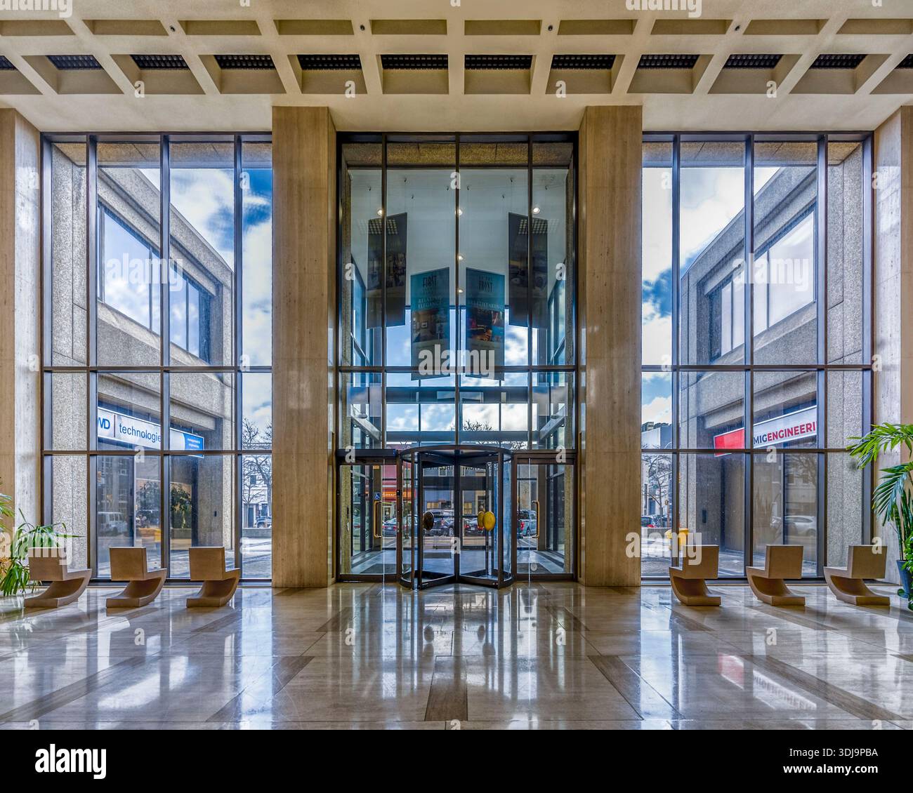 Lobby aziendale moderna e simmetrica con facciata in vetro, porte girevoli, pavimenti in marmo lucido e forti linee architettoniche geometriche. Foto Stock