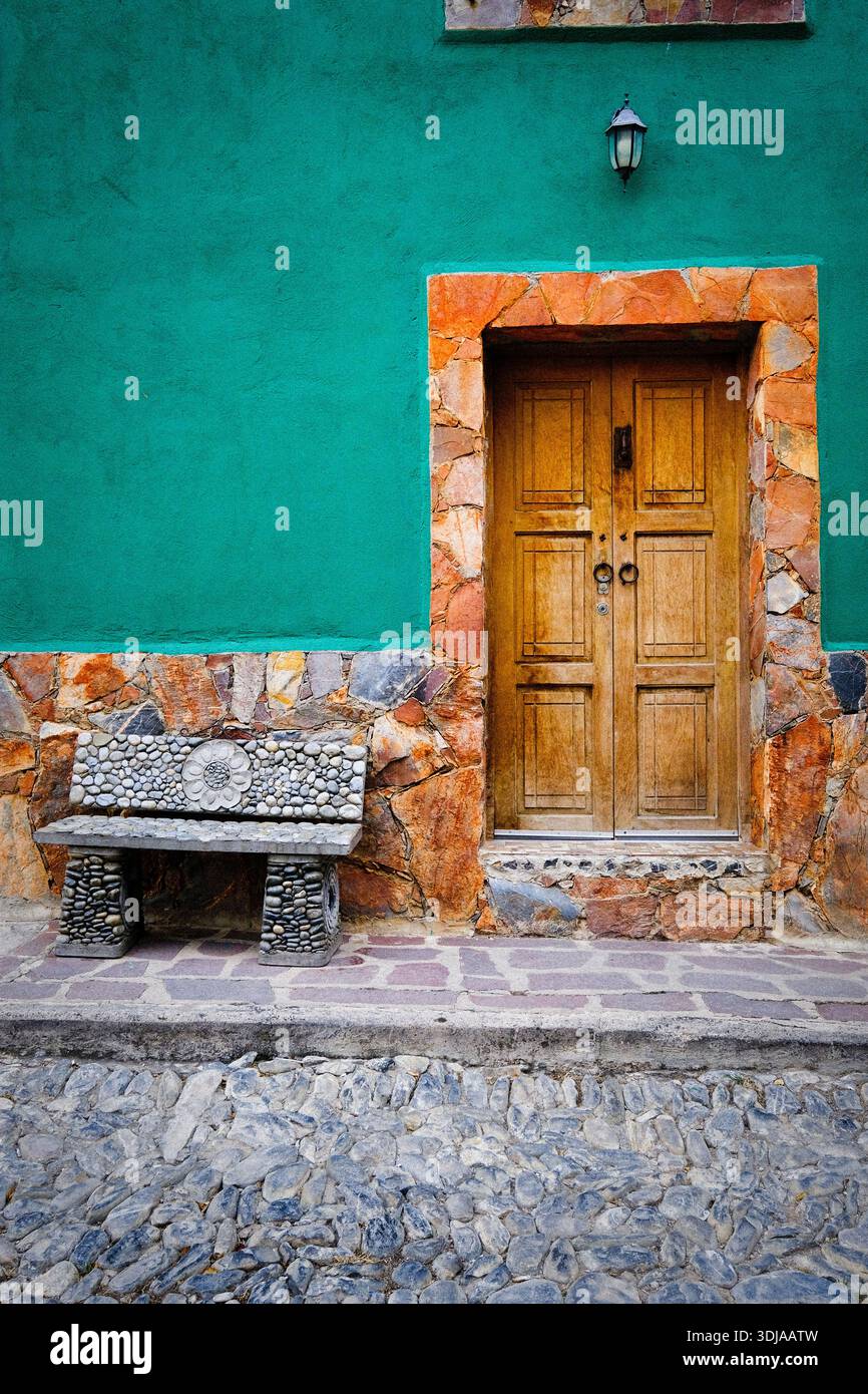 Un'invitante porta in legno con una panchina di pietra di fronte ad una vibrante parete verde, che aggiunge fascino al paesaggio architettonico Foto Stock