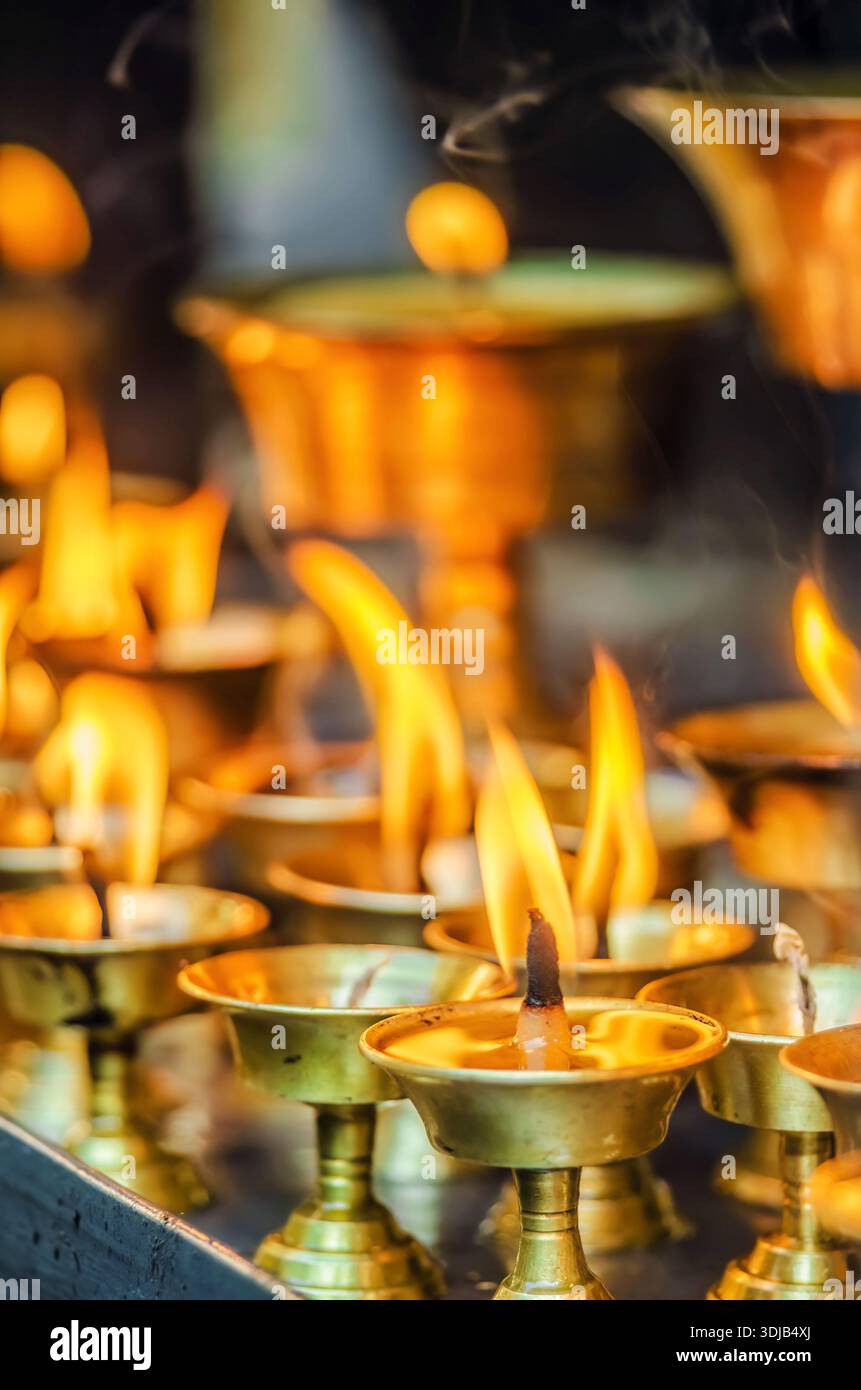 Più lampade a olio in ottone con fiamme accese si siedono vicine tra loro, emettendo una calda luce soffusa in un ambiente rituale Foto Stock