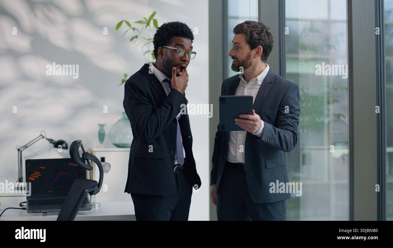 Due uomini d'affari multietnici di diversità colleghi discutono il successo online guardando un tablet digitale stupito di buone notizie multirazziale Foto Stock