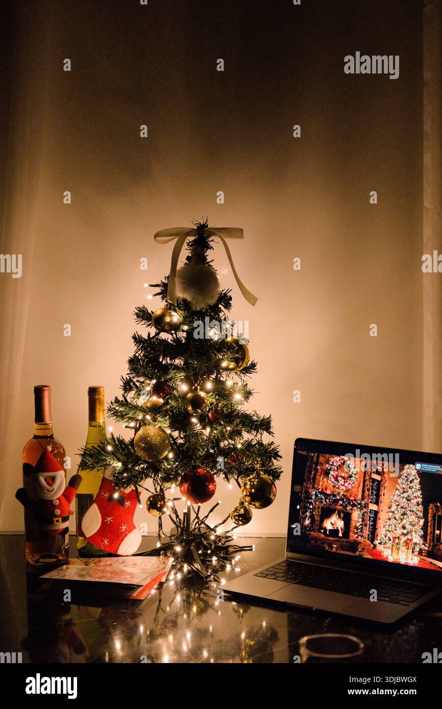 Accogliente scenario natalizio al coperto con un albero decorato, calde luci a corda e decorazioni natalizie su un tavolo. Foto Stock