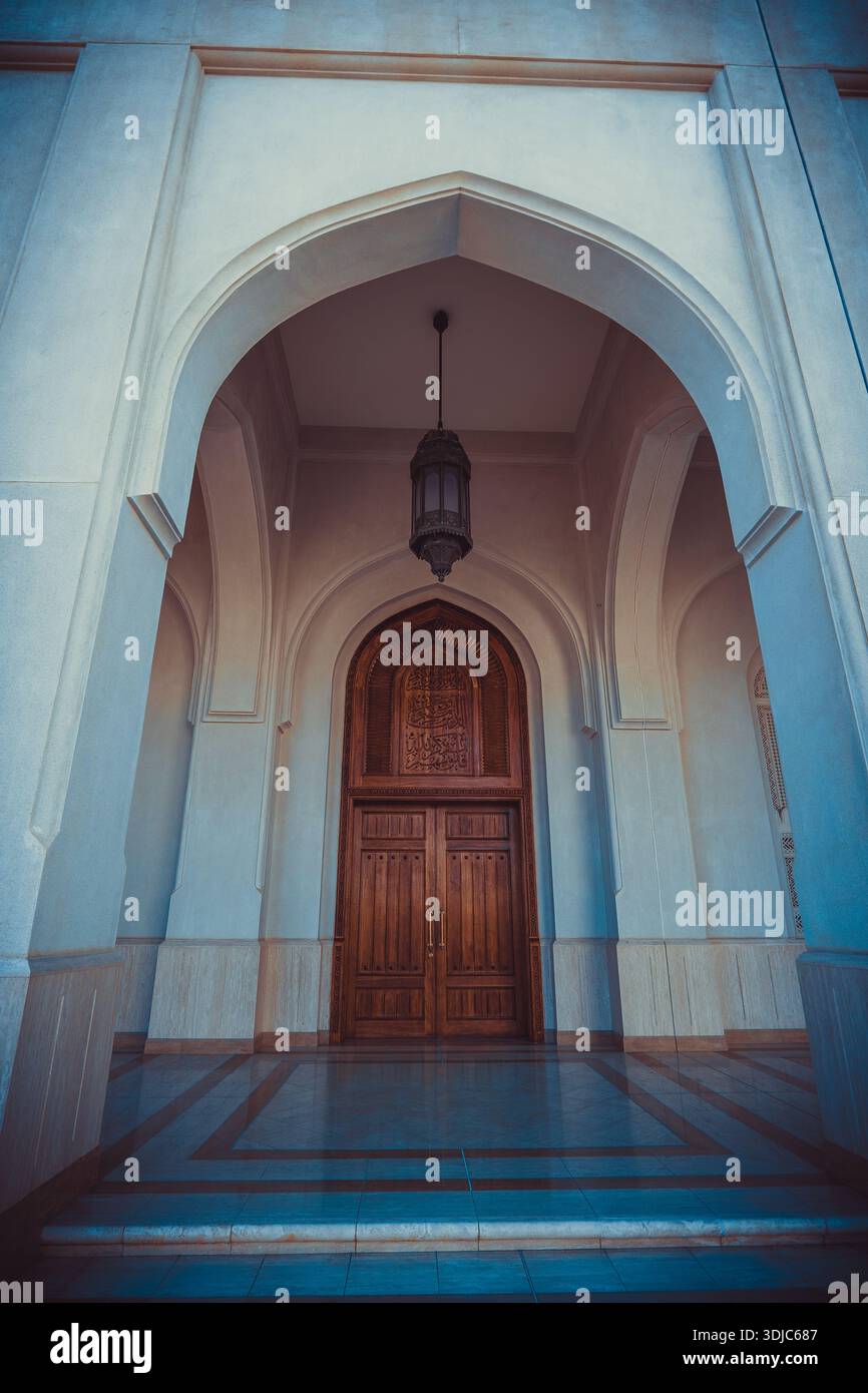 Una vista dall'angolo basso di una grande moschea d'ingresso a Salalah, Oman, caratterizzata da molteplici strutture ad arco bianche che conducono ad un legno scuro splendidamente intagliato Foto Stock