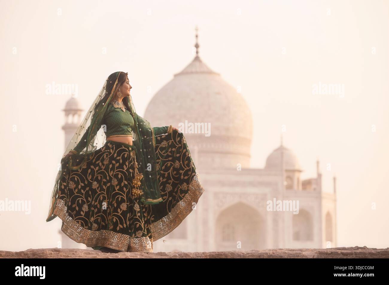 Vista laterale di una giovane donna in un sari che tiene l'orlo del vestito davanti al Taj Mahal al tramonto, Agra, Uttar Pradesh, India, Foto Stock